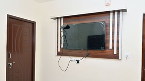 A room with a wooden door, a wall-mounted television, and a power outlet. - HOTEL SIDDVEER GRAND (Guntur)