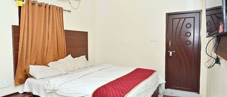 A bedroom with a bed, a ceiling fan, an air conditioning unit, a wooden nightstand, and a door.
