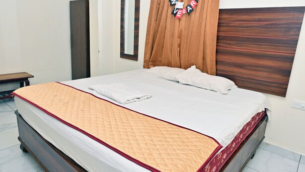 A neatly made bed with a quilted cover and pillows, a wooden headboard, a mirror, and a wall-mounted 'Happy Anniversary' decoration. - HOTEL SIDDVEER GRAND (Guntur)