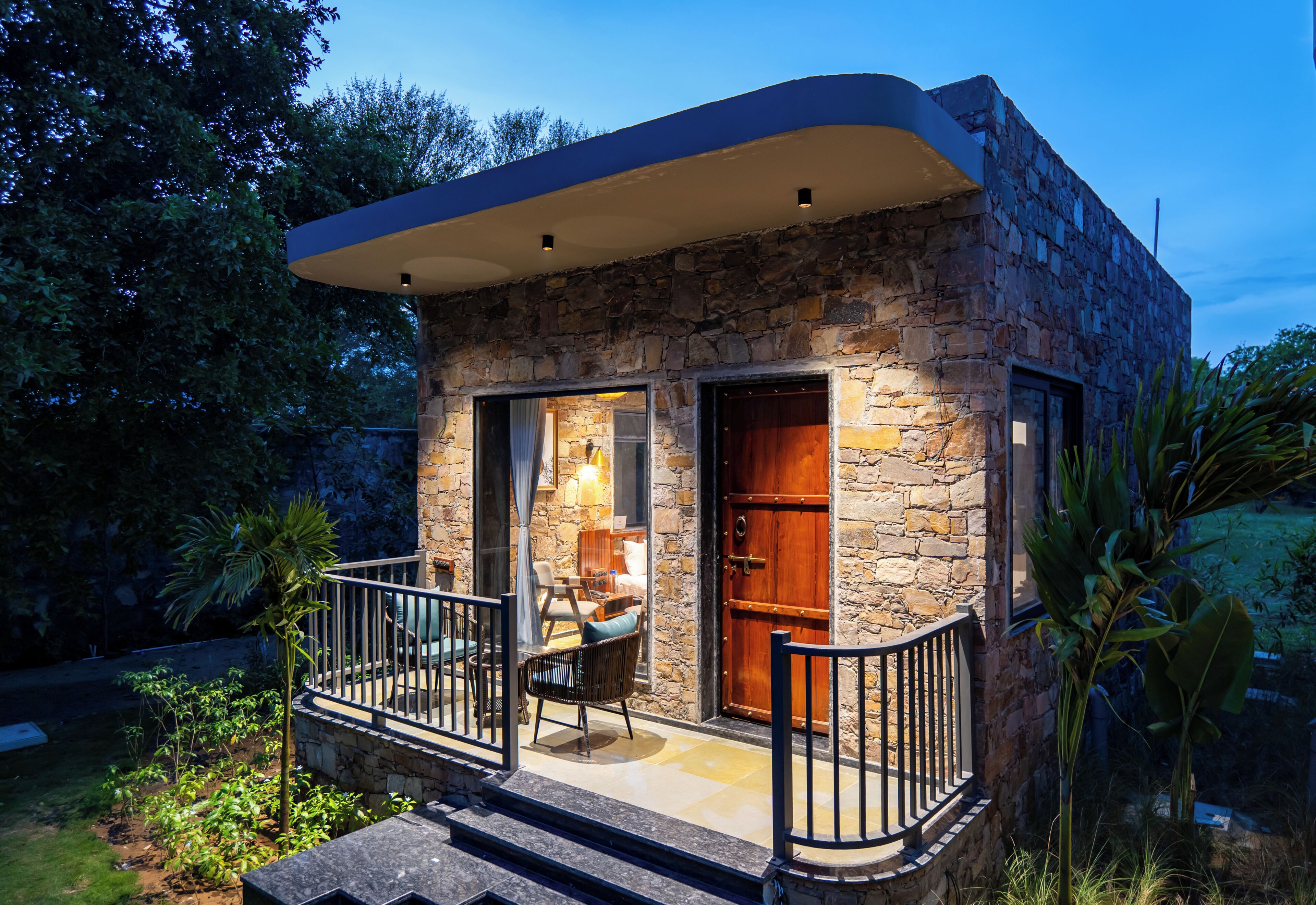A stone house with a balcony, a wooden door, and a small seating area with a table and chairs.