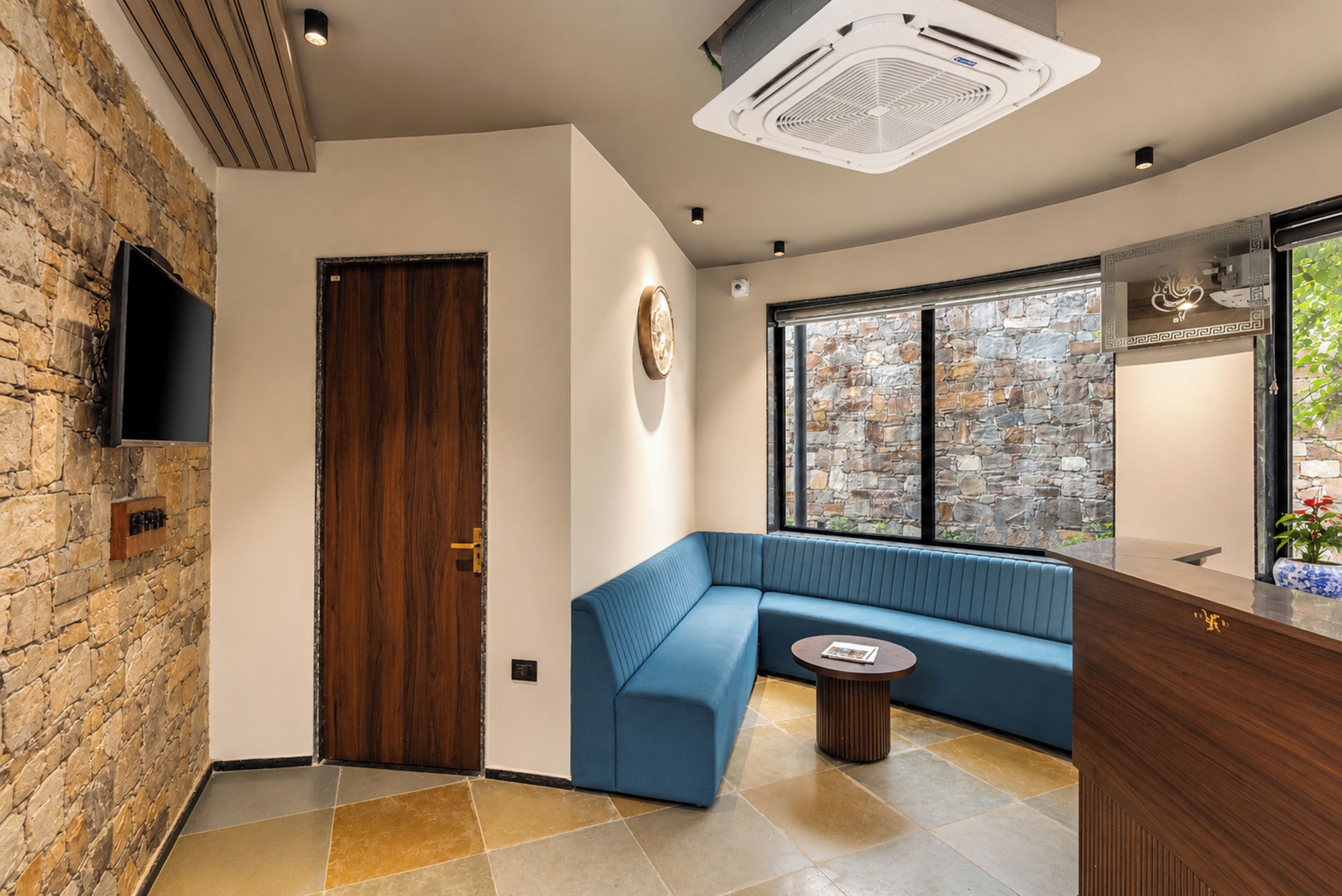 A modern interior with a stone wall, a wooden door, a blue sofa, a small round table, and a flat-screen TV mounted on the wall.