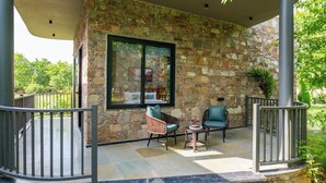 A stone exterior wall with a large window, outdoor seating with cushions, and a metal railing.