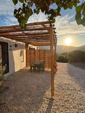 A covered outdoor seating area with a pergola, a table with chairs, and a gravel ground.