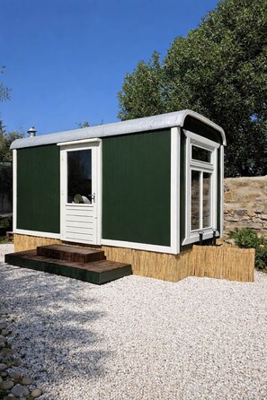 Une petite maison mobile d’un seul étage, peinte en vert et en blanc, avec une porte d’entrée et une fenêtre.