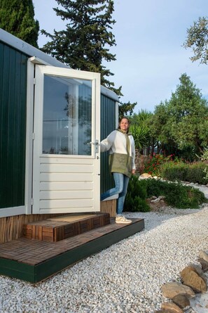 Une personne qui monte sur une terrasse en bois à l’extérieur d’un bâtiment doté d’une porte blanche.