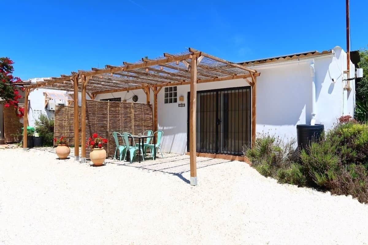 A covered outdoor seating area with a pergola, a table with chairs, and potted plants.