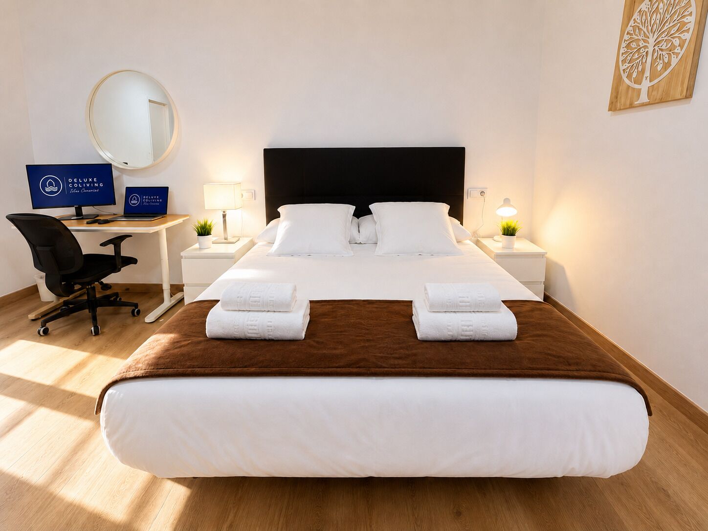 Una habitación de hotel con una cama grande, un escritorio con computadora, una silla y un espejo redondo.