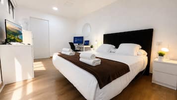 Una habitación de hotel con cama, escritorio, computadora, televisor y lámpara de noche.