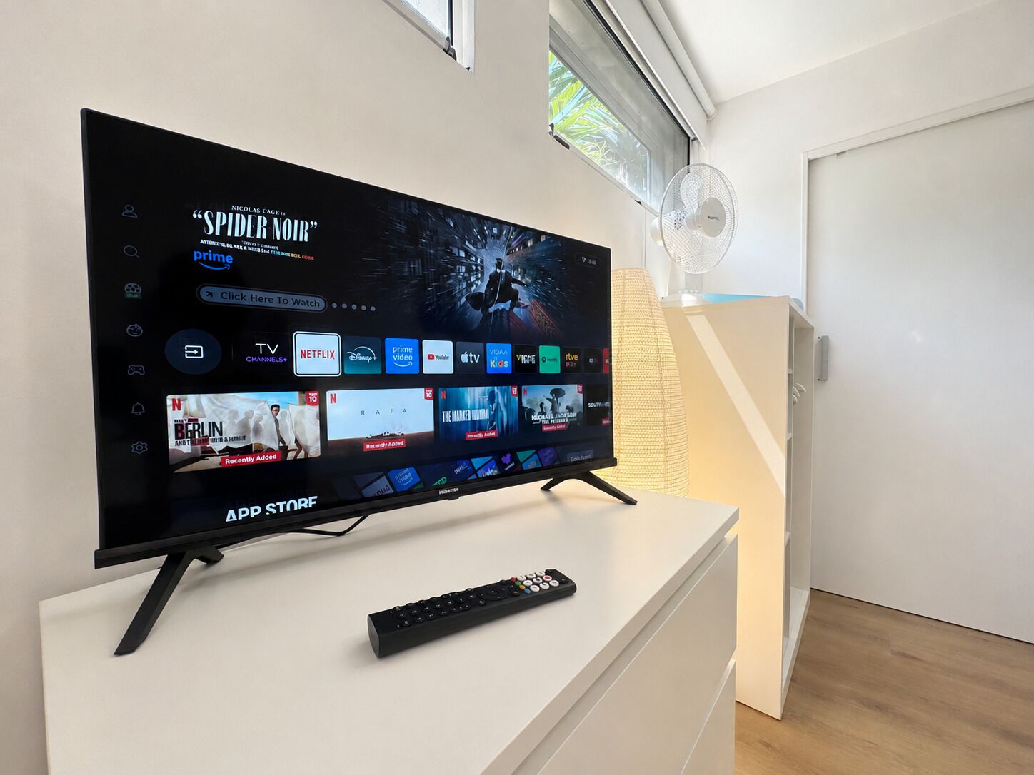 A flat-screen TV on a white stand with a remote control beside it.