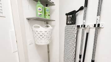Esquina de una habitación con un trapeador, escoba, cesta de ropa y productos de limpieza en un estante adosado a la pared.