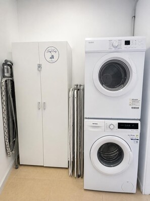 Une buanderie équipée d’un lave-linge blanc, d’un sèche-linge et d’un meuble sur lequel est apposée une étiquette indiquant : « Taches uniquement ».