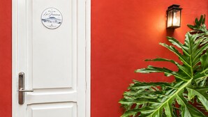 A white door with a room sticker, a potted plant, and a wall-mounted light fixture.