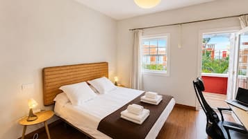 A hotel room with a bed, bedside lamp, desk with chair, and a view of buildings through the window.