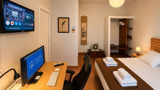 A hotel room with a desk, computer, bed, and a TV displaying HBO max and Apple TV apps.