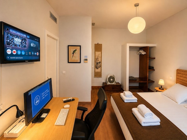 A hotel room with a desk, computer, bed, and a TV displaying HBO max and Apple TV apps.