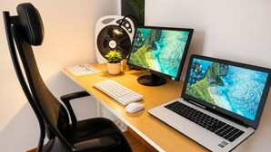 A workspace with a chair, desk, two monitors, a laptop, a keyboard, a mouse, and a fan.