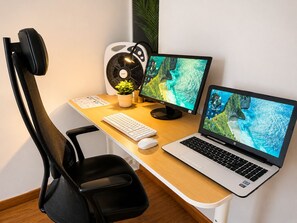 A workspace with a chair, desk, two monitors, a laptop, a keyboard, a mouse, and a fan.