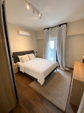 Ein Schlafzimmer mit einem Bett, Nachttischen, einer Klimaanlage und einem Fenster mit Vorhängen.