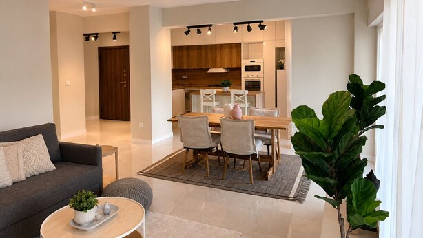 A modern living room with a sofa, coffee table, and dining area with chairs and a table. - Solea by Neuvel (Glyfada)