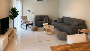 A modern living room with a flat-screen TV, a sofa, a chair, a coffee table, and a potted plant. - Solea by Neuvel (Glyfada)