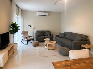Ein modernes Wohnzimmer mit Flachbildfernseher, einer Couch, einem Sessel, einem Couchtisch und einer Topfpflanze.