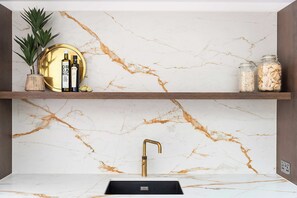 A kitchen with marble countertops, a gold-colored faucet, and two shelves with various items. - Stylish 4BR Victorian Home Parking with EV Charger (Cambridgeshire)