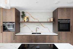 A modern kitchen with a marble backsplash, stainless steel appliances, and wooden cabinetry. - Stylish 4BR Victorian Home Parking with EV Charger (Cambridgeshire)