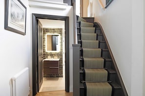 A staircase with a handrail and carpeted steps leading to a bathroom with a tiled wall and a mirror. - Stylish 4BR Victorian Home Parking with EV Charger (Cambridgeshire)