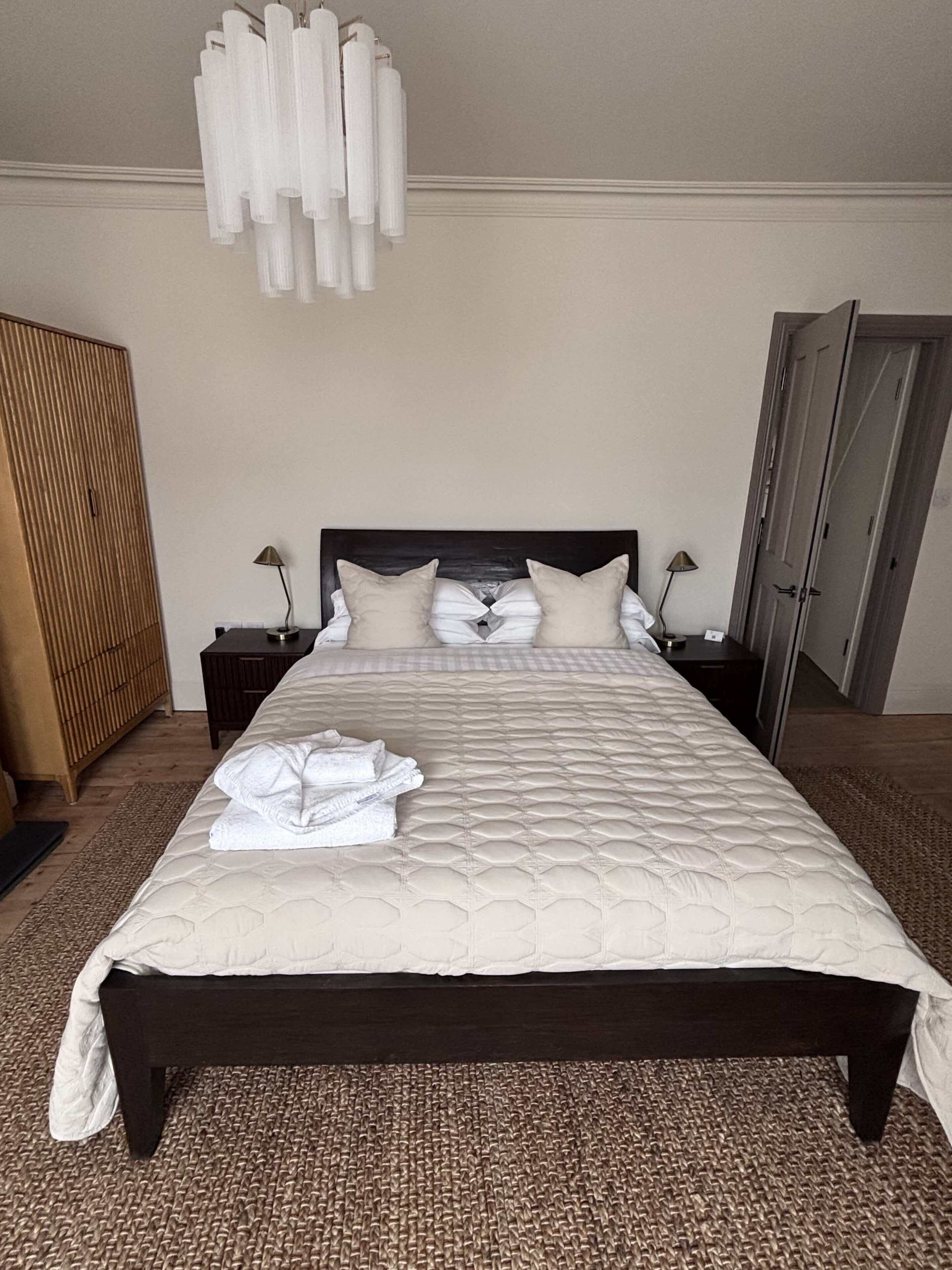 A neatly made bed with a quilted headboard, two bedside lamps, and a folded towel on the bed.