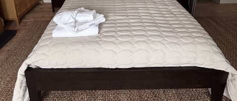 A neatly made bed with a quilted headboard, two bedside lamps, and a folded towel on the bed.