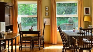 Un comedor con una mesa y sillas, dos ventanas con cortinas y vistas a la vegetación.