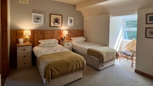 Un dormitorio con dos camas, cabeceros de madera, mesitas de noche con lámparas, cuadros enmarcados en la pared y una ventana con vistas.