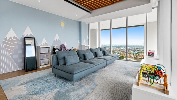 A modern living room with a large gray sofa, a wooden ceiling, and a city view through large windows. - Jasen by Kozystay - Alam Sutera (Tangerang)