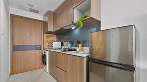A modern kitchen with wooden cabinets, a stainless steel refrigerator, a built-in oven, and a microwave. - Jasen by Kozystay - Alam Sutera (Tangerang)