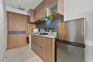 A modern kitchen with wooden cabinets, a stainless steel refrigerator, a built-in oven, and a microwave. - Jasen by Kozystay - Alam Sutera (Tangerang)