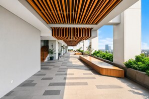 A modern outdoor corridor with a wooden slatted ceiling, potted plants, and a view of the cityscape. - Jasen by Kozystay - Alam Sutera (Tangerang)