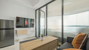 A modern kitchen with a built-in refrigerator, a wooden dining table, and a sofa with a cushion. - Jasen by Kozystay - Alam Sutera (Tangerang)