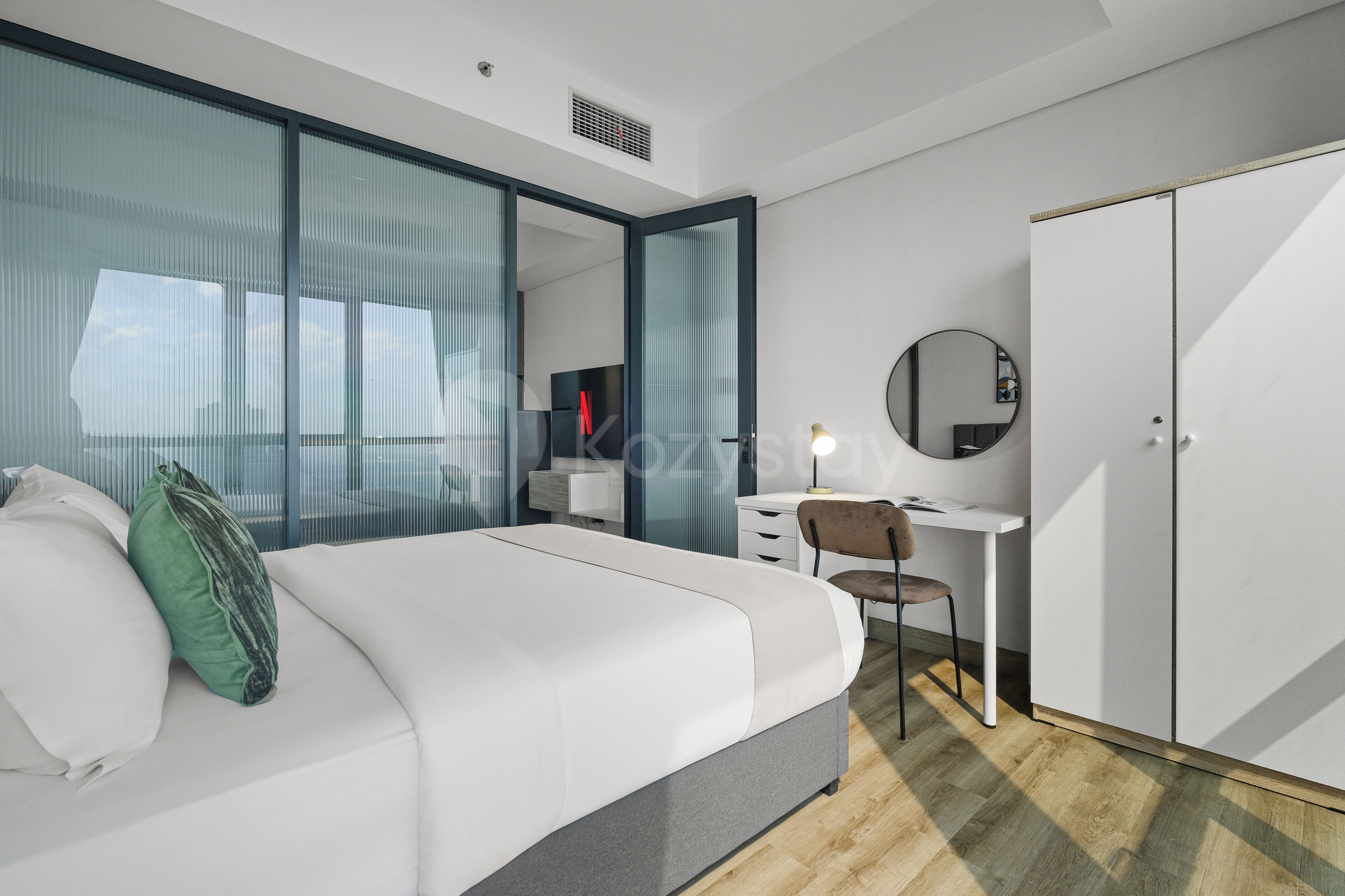 Habitació d'hotel moderna amb llit, escriptori, cadira, armari i una finestra gran amb cortines.