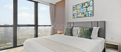 Una habitación de hotel moderna con una cama grande, vistas a la ciudad, un cuadro en la pared y una mesita de noche.