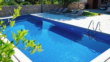 Uma piscina retangular com água azul cristalina, cercada por um muro de pedra e um deck revestido com espreguiçadeiras.