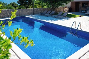 Una piscina rectangular amb aigua turquesa cristal·lina, envoltada per una paret de pedra i un solàrium amb gandules.