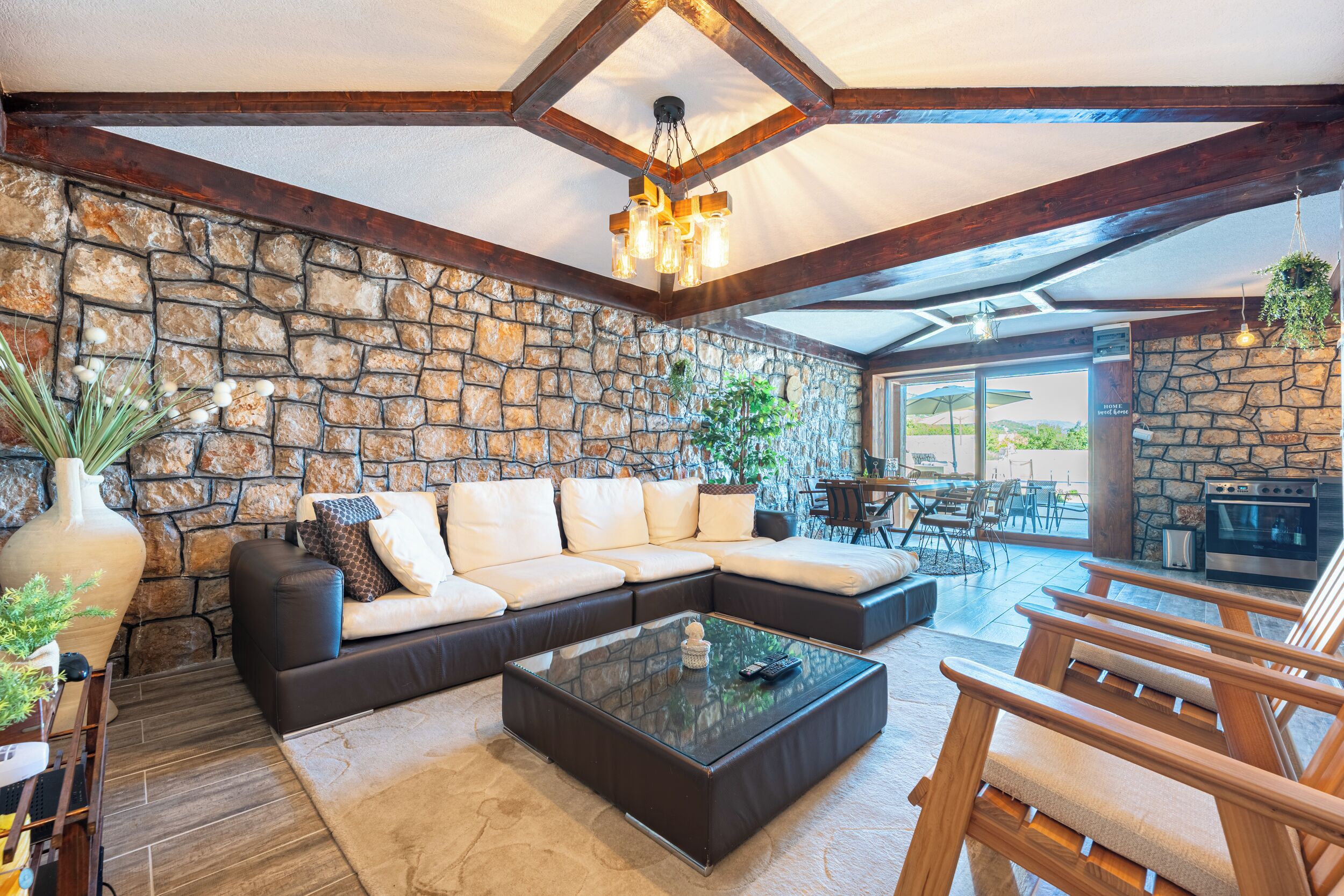 A modern living room with a stone wall, a sectional sofa, a glass coffee table, and a wooden ceiling.