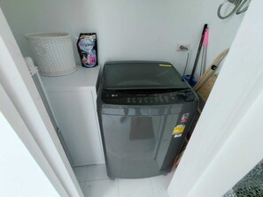 A compact washing machine in a small laundry area with a basket and a hygiene product on the wall. - Kamala Jungle Suite 80m² Balcony, 2 Pools, Gym & Sauna Fast Fiber WiFi (Kamala, Kathu)