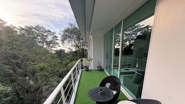 A balcony with artificial grass, a table, and two chairs. - Kamala Jungle Suite 80m² Balcony, 2 Pools, Gym & Sauna Fast Fiber WiFi (Kamala, Kathu)