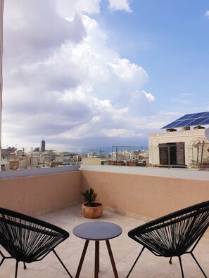 A rooftop terrace with two chairs, a small table, and a potted plant.
