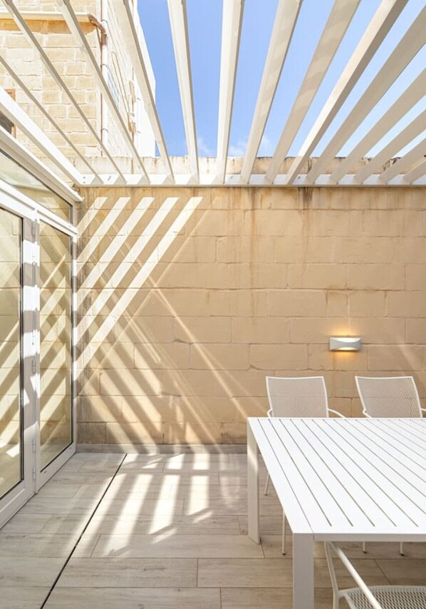 A patio area with a table and chairs, a wall with a light fixture, and a view of the sky.