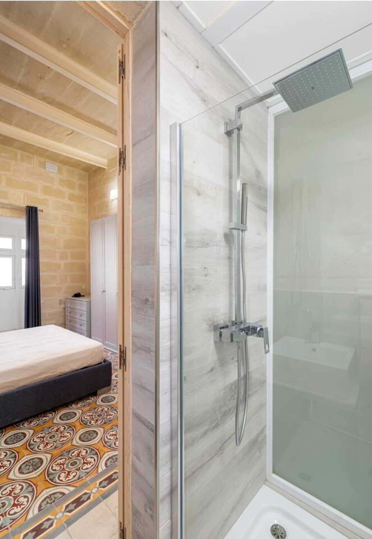 Une chambre avec un lit, une douche dotée d’une porte en verre et un sol à motifs.