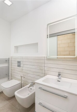 Et moderne badeværelse med toiletbidét, vask og spejl.
