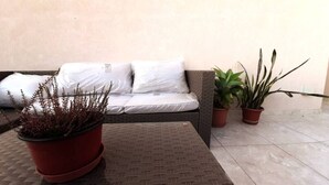 Ein rattangewobenes Sofa mit weißen Kissen, ein Flecht-Tisch und Blumentöpfe.