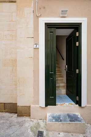 A building entrance with a green door, a white wall, and a visible staircase leading inside.